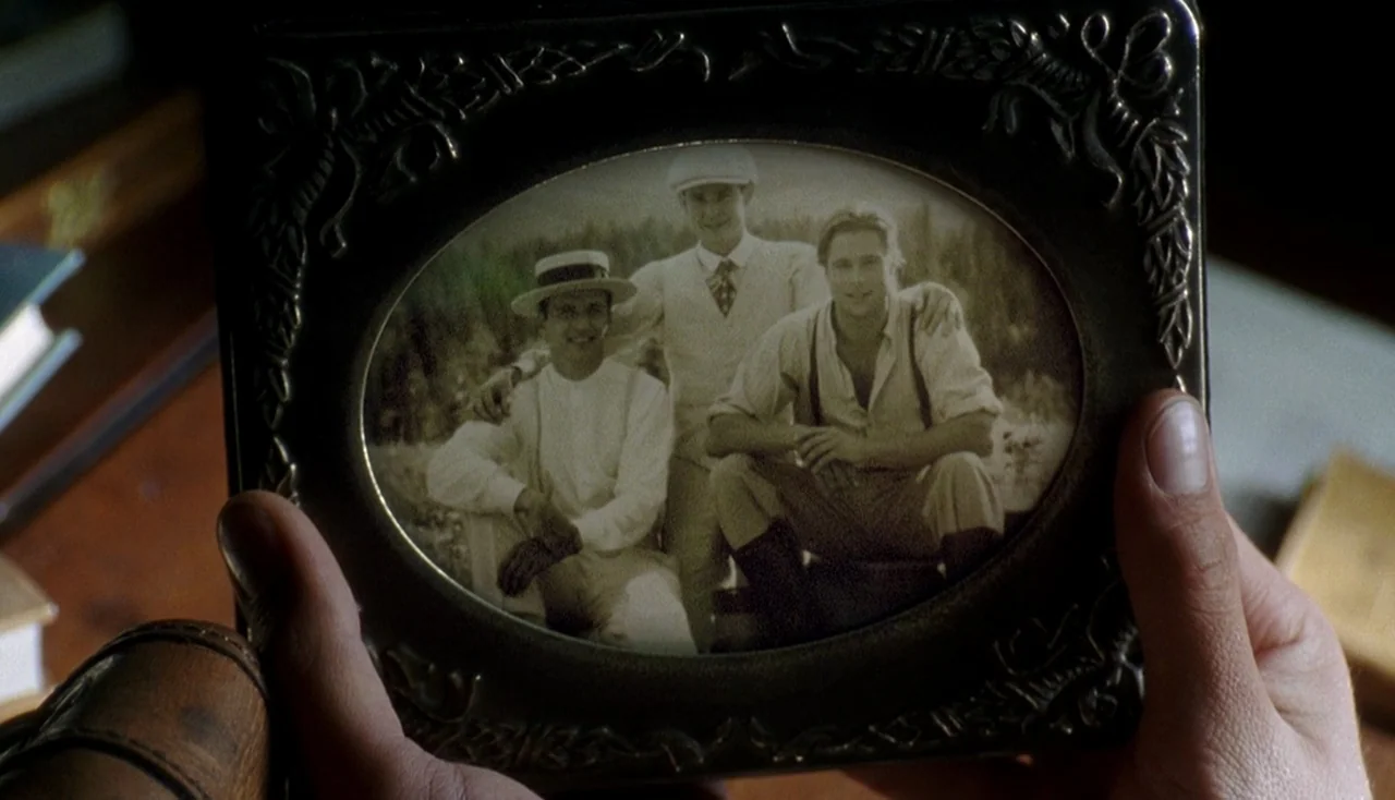 Legends of the Fall (1994) movie still: closeup — An oval metal frame holds a vintage photograph of three men in formal attire. The frame is held in…