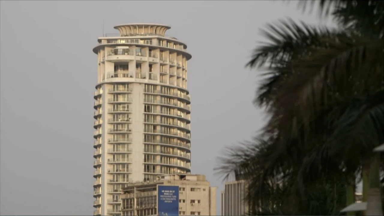 The FIFA Family: A Love Story (2017) movie still: establishing — A tall, modern cylindrical apartment building rises above older, shorter…