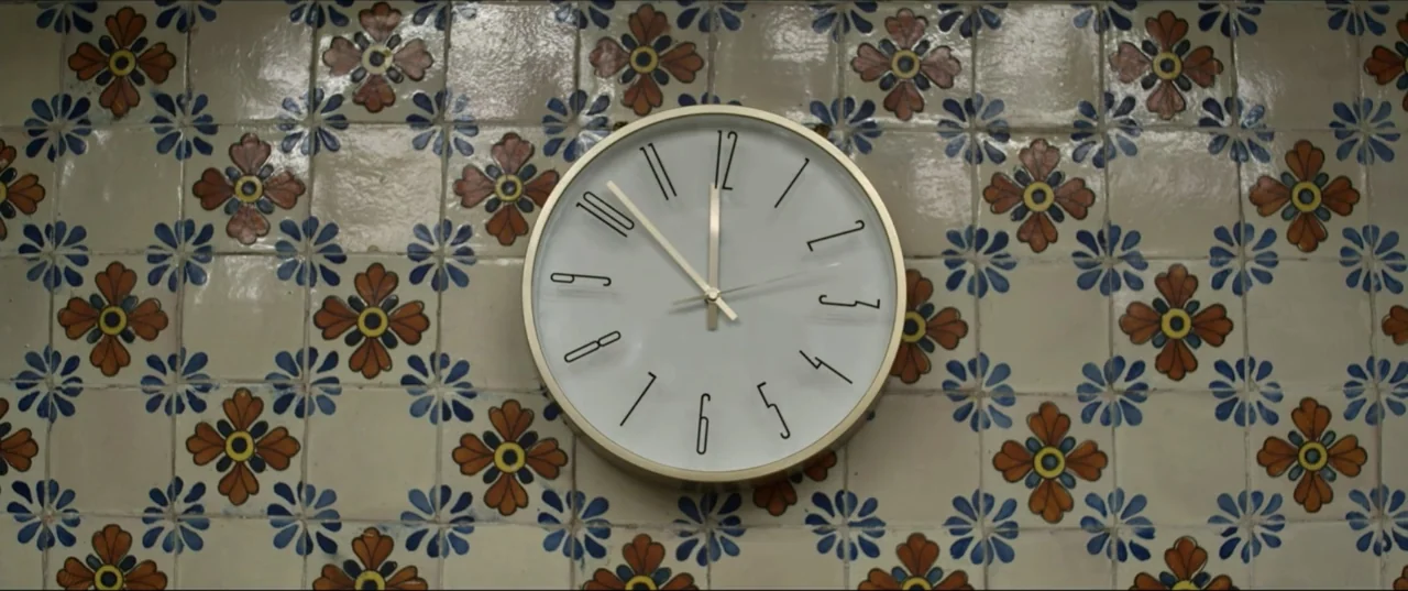 Can't Quit Mom (2022) movie still: closeup — A decorative analog clock is centered against a wall of vintage floral tiles. The clock hands indicate…