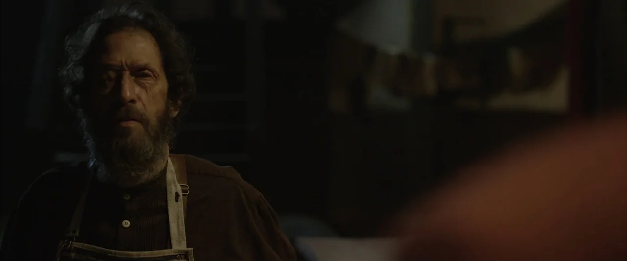 Ghosts of the Ozarks (2022) movie still: medium — A dimly lit, shadow-filled workshop with indiscernible objects resting in the background. An older…