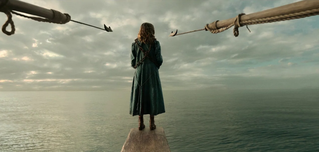 Peter Pan & Wendy (2023) movie still: fullbody — A person stands on a wooden plank extending over a calm, vast gray sea. The sky above is filled…