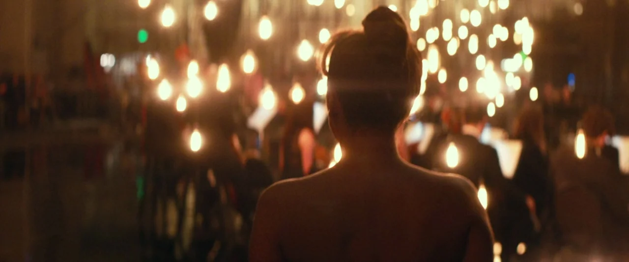 A Star Is Born (2018) movie still: medium — An out-of-focus dark space is filled with hundreds of suspended, glowing light bulbs. A woman seen from…