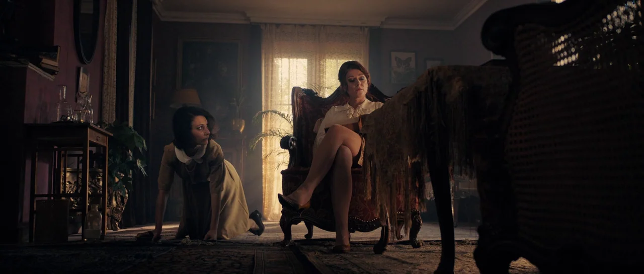 The Duke of Burgundy (2014) movie still: wide — A cluttered mid-century living room is filled with dark wooden furniture and ornate carpets. One…