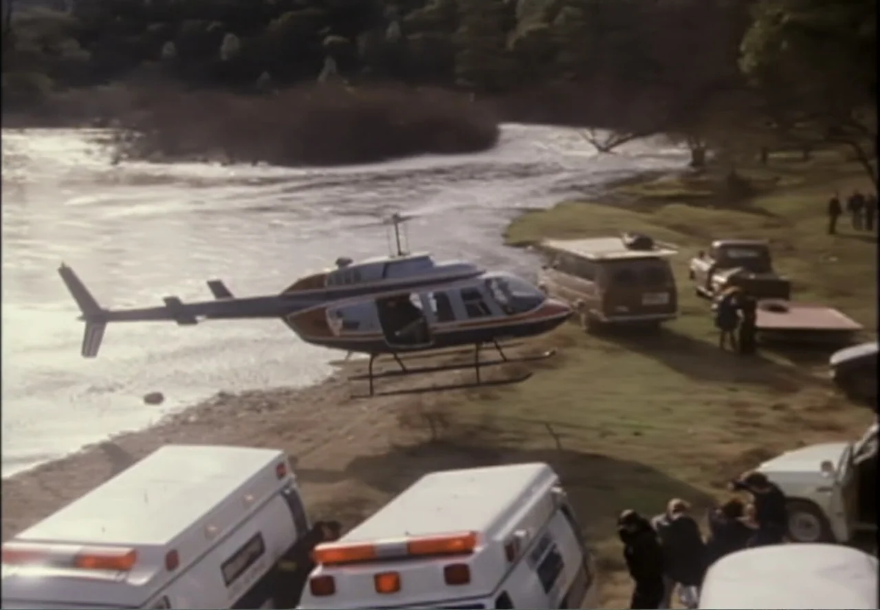 White Mile (1994) movie still: wide — A helicopter lands on the grassy bank of a wide, flowing river. Several white emergency vehicles and a group…