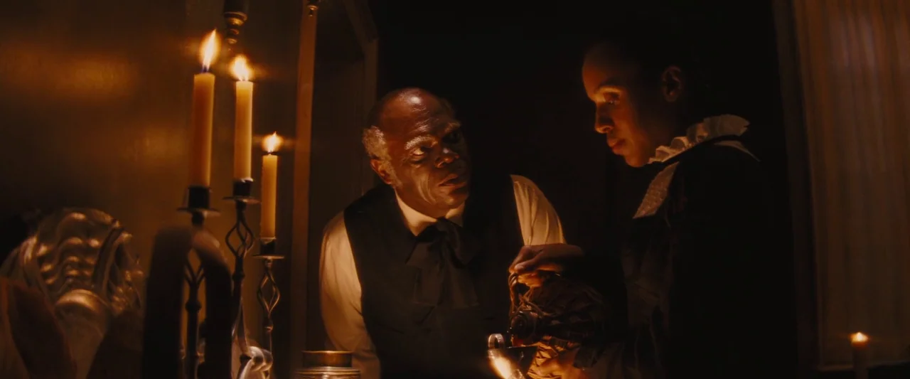 Django Unchained (2012) movie still: medium — A dimly lit 19th-century room contains wooden furniture and lit candles in metallic holders. A woman…