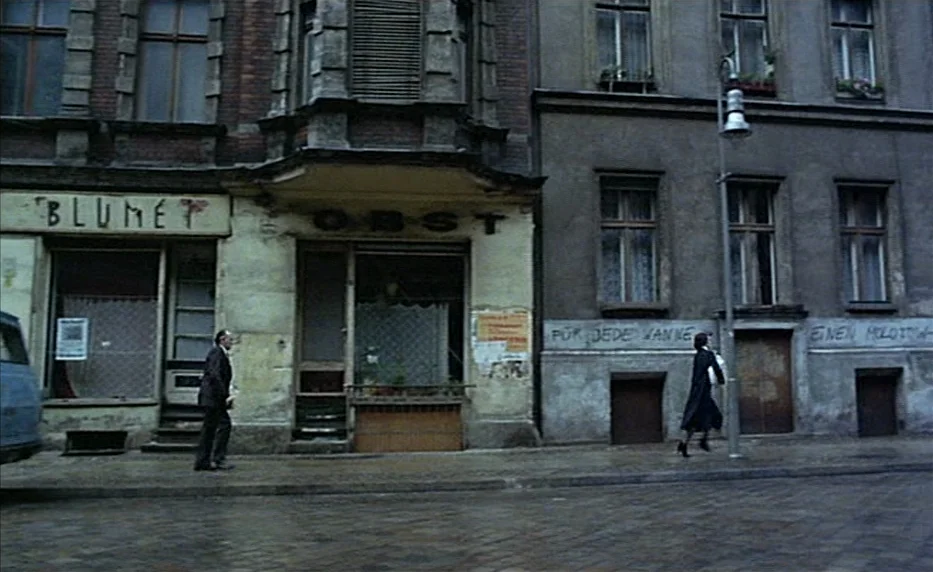 Possession (1981) movie still: wide — A European city street features weathered multi-story buildings with weathered brick and concrete facades. A…