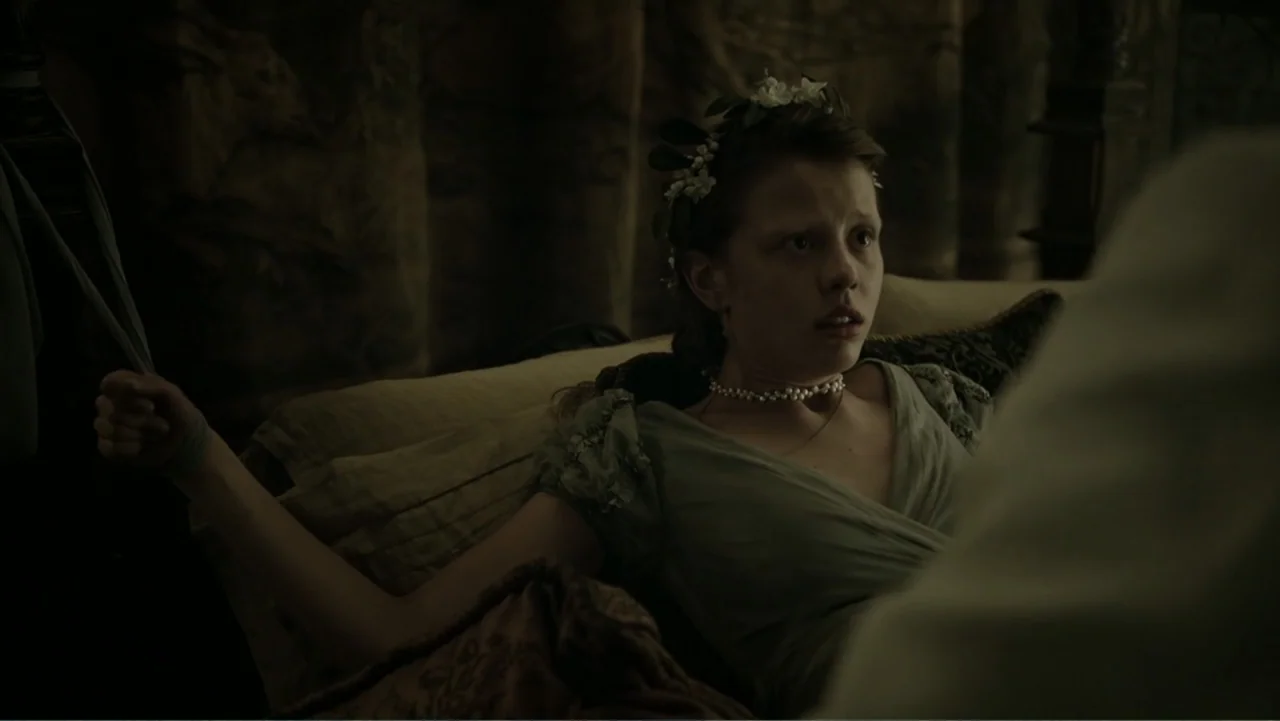 A Cure for Wellness (2017) movie still: medium — A dimly lit historical bedroom features heavy curtains and dark, textured bedding. A young woman in…