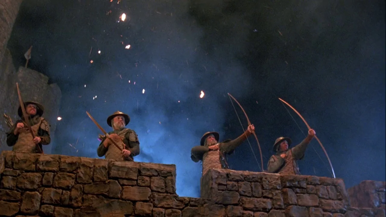 Army of Darkness (1992) movie still: wide — Four archers stand on stone ramparts at night amidst floating orange embers and smoke. The soldiers aim…