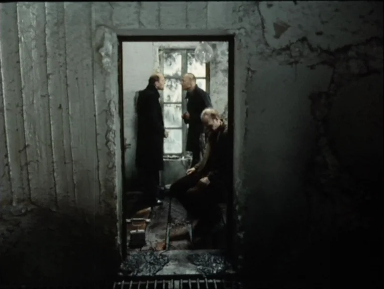 Stalker (1979) movie still: medium — A decaying, industrial-looking room with peeling paint and concrete walls viewed through an open doorway. Three…