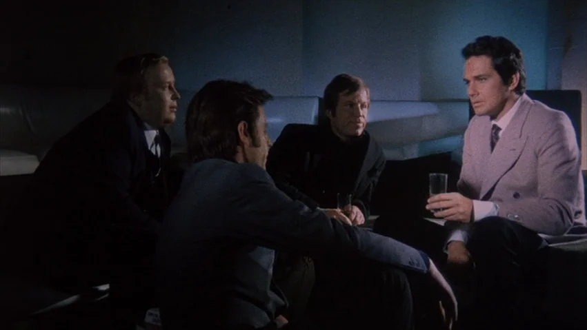 Four Times that Night (1971) movie still: medium — A dimly lit lounge booth features four men sitting in conversation. One man in a light jacket…