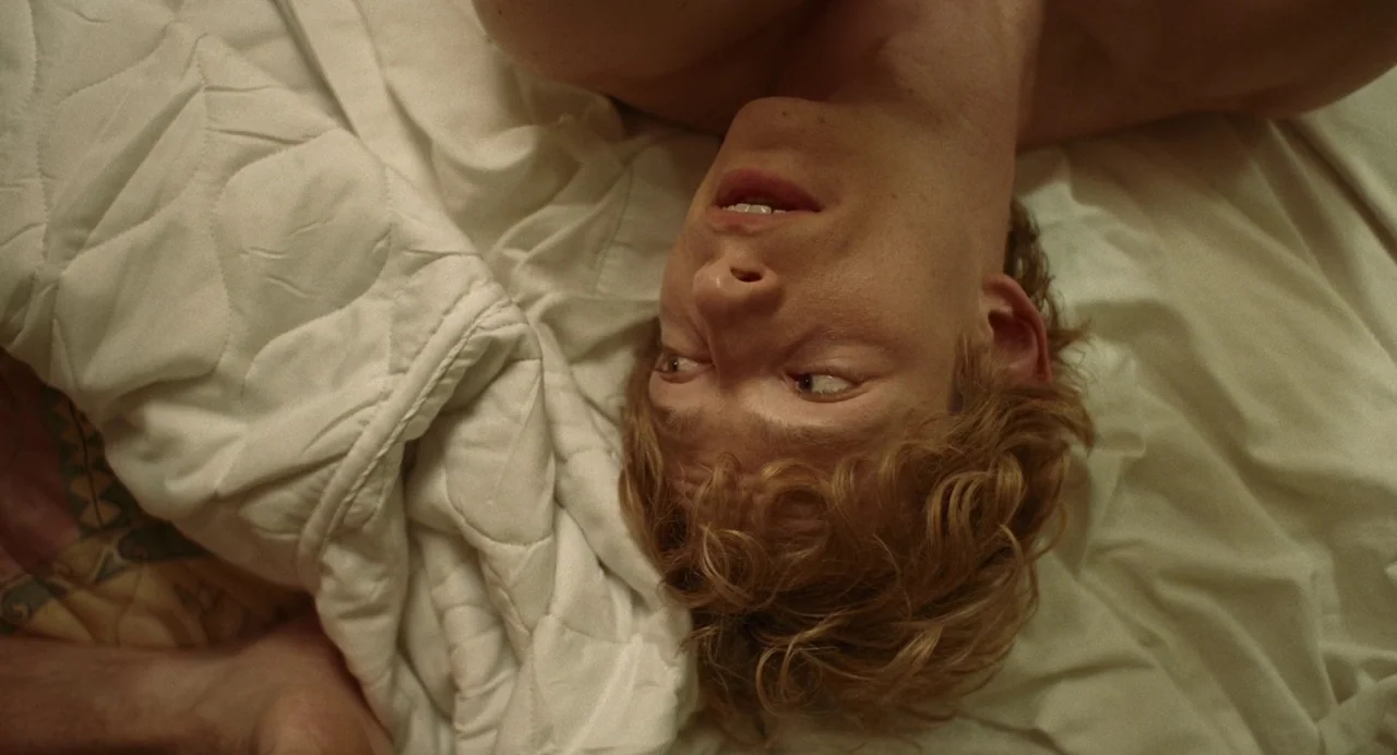 Challengers (2024) movie still: closeup — A person lies on a white quilted blanket on a bed. The individual rests their head back against the…