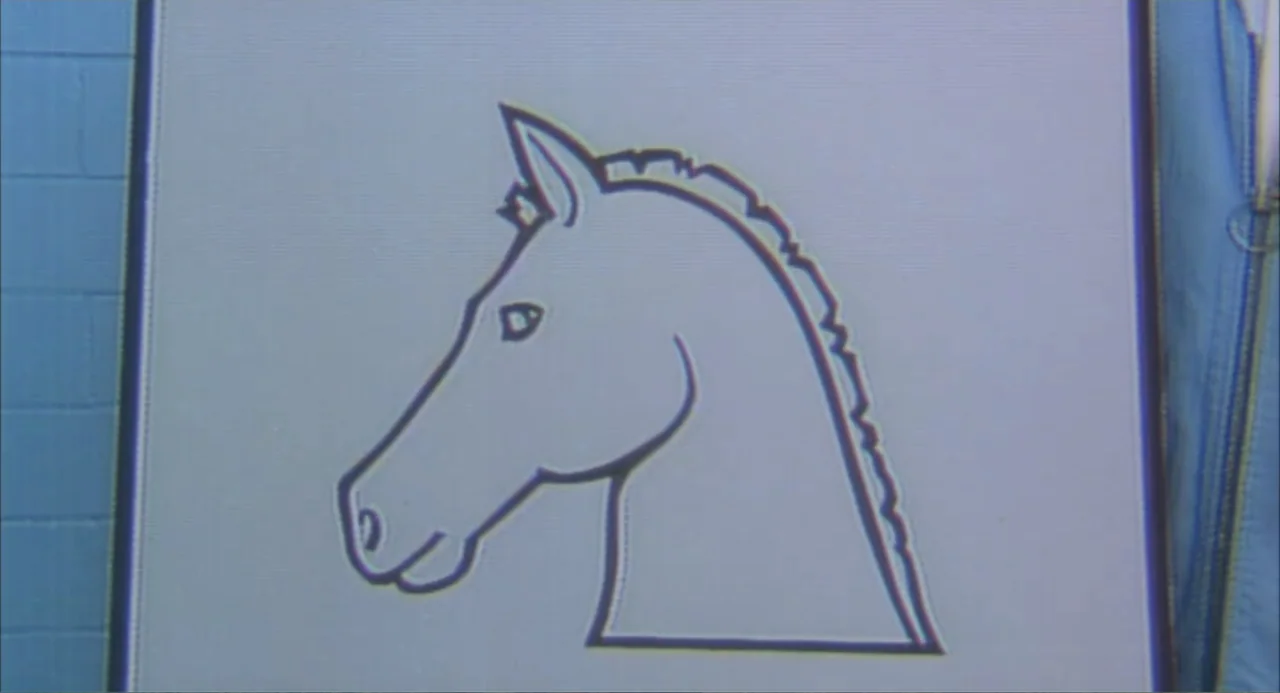 Making Mr. Right (1987) movie still: closeup — A simplified line drawing of a horse head occupies the center of a flat board. To the right, the edge…