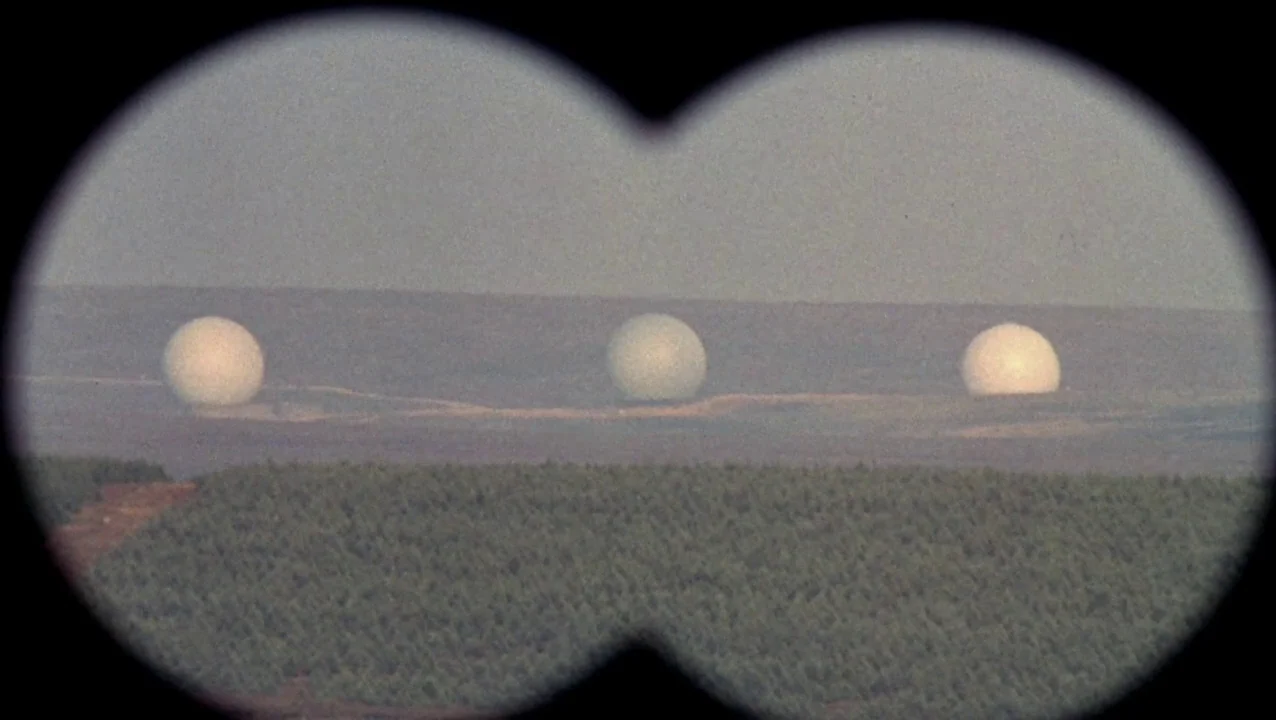 O Lucky Man! (1973) movie still: wide — A vast, barren desert landscape stretches toward the horizon under a hazy sky. Three large white radar domes…