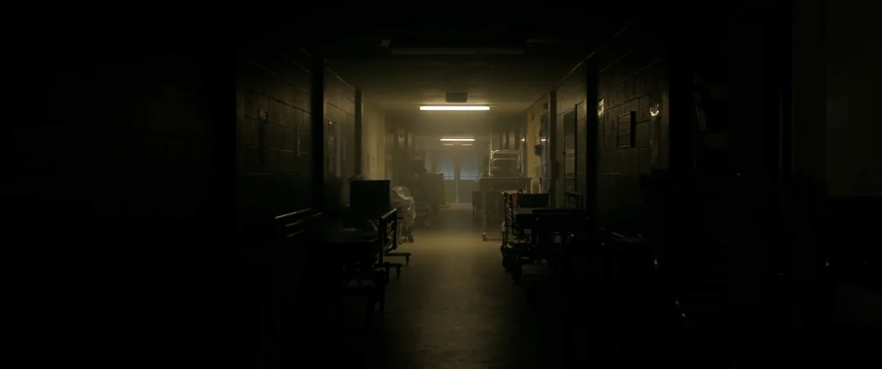 The Void (2016) movie still: wide — A long, dark hospital corridor features block walls and multiple pieces of medical equipment. A single…