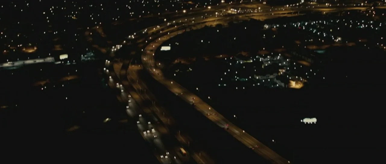 Contraband (2012) movie still: establishing — An aerial night view of a sprawling highway interchange with multiple lanes of traffic. Vehicles move…