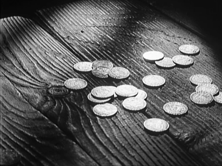 Oliver Twist (1948) movie still: closeup — A collection of metallic coins is scattered across weathered, dark wooden planks. The surface features…