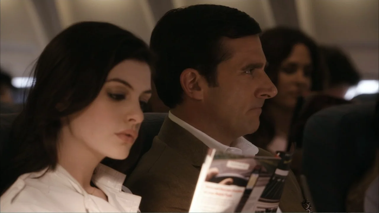 Get Smart (2008) movie still: medium — The interior of an airplane cabin shows passengers seated in rows. A man and a woman occupy adjacent seats…
