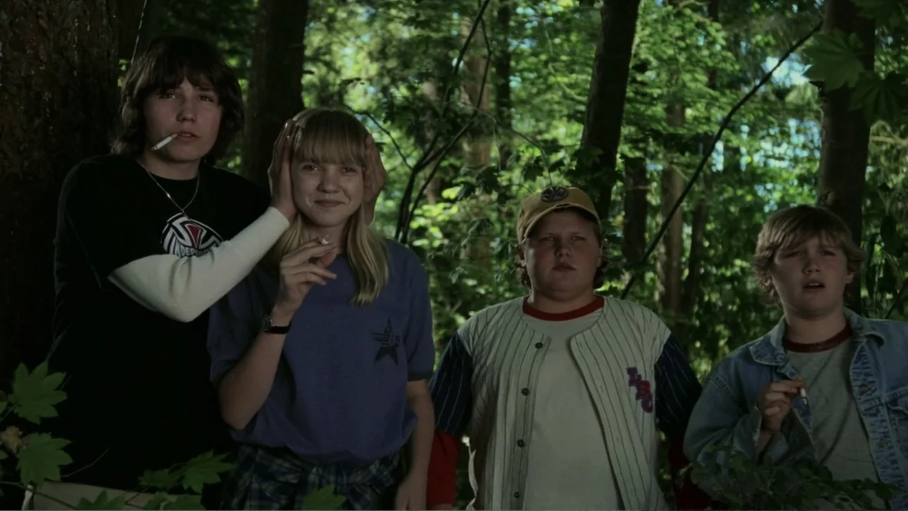 The Butterfly Effect (2004) movie still: medium — Dense woodland setting with tall trees and dappled sunlight filtering through green foliage. Four…