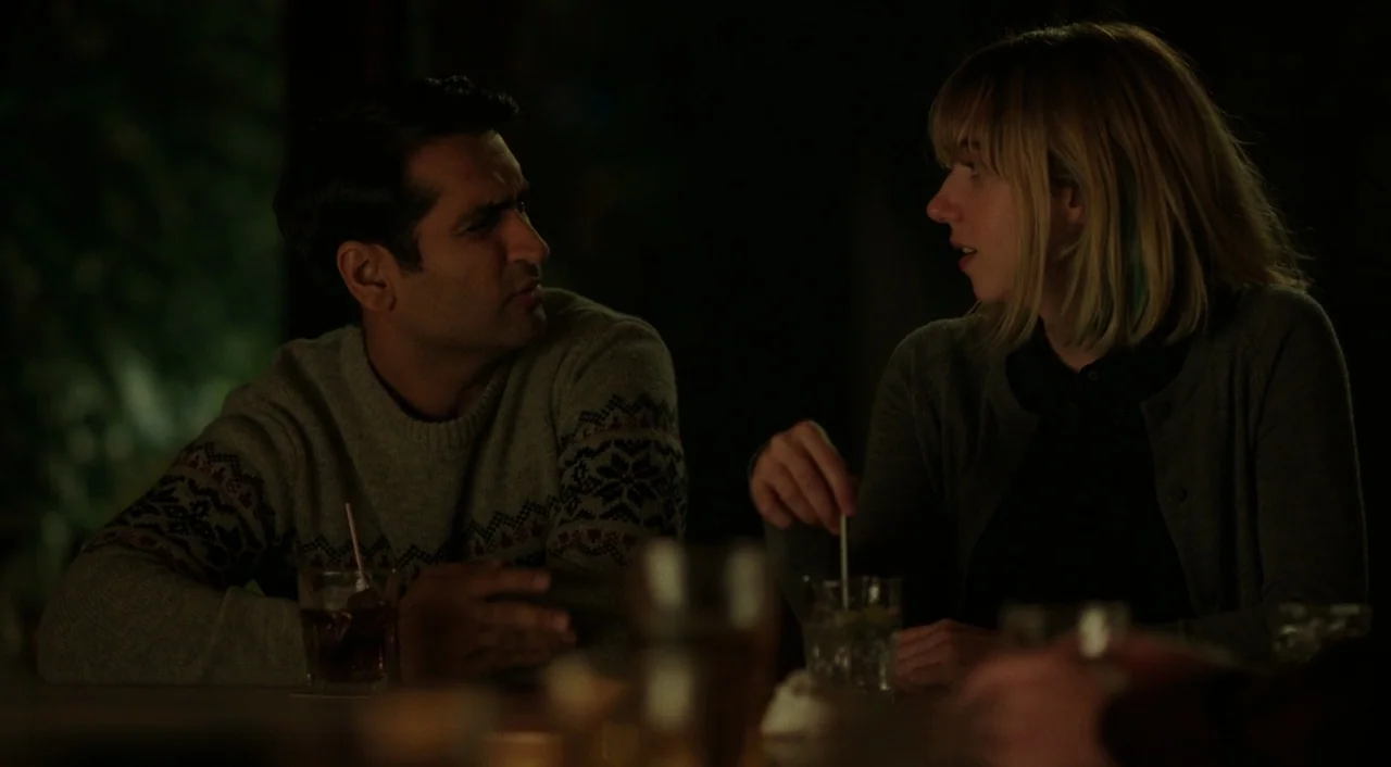 The Big Sick (2017) movie still: medium — A dimly lit bar at night with dark shadows surrounding two seated people. The man and woman sit across…