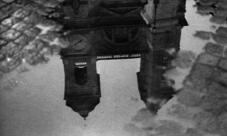 The Girl Who Knew Too Much (1963) movie still: wide — A reflection of a church tower is visible in a large rain puddle. The surrounding ground…