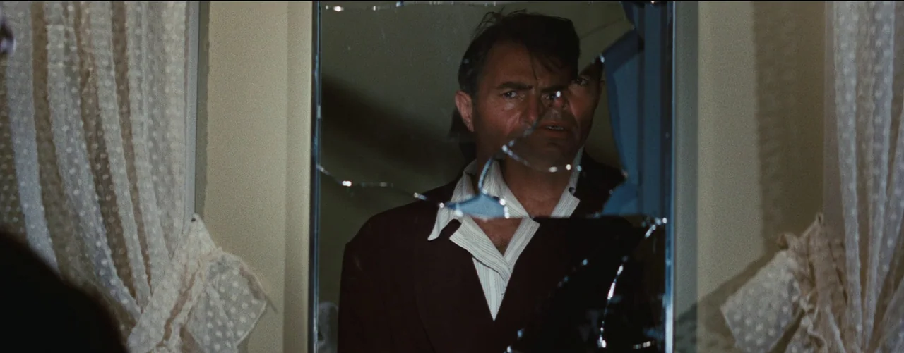 Bigger Than Life (1956) movie still: medium — A man looks into a shattered mirror inside a room with translucent lace curtains. The reflection of…