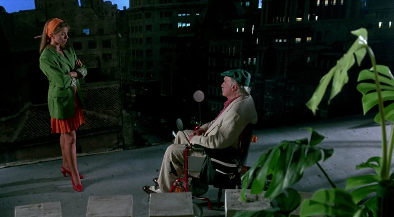 Tie Me Up! Tie Me Down! (1989) movie still: fullbody — A rooftop terrace at night overlooks a dark urban cityscape with distant building windows. A…