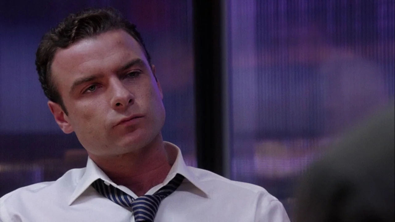 The Manchurian Candidate (2004) movie still: closeup — A man sits inside a workspace with purple light visible behind frosted glass panels. He looks…