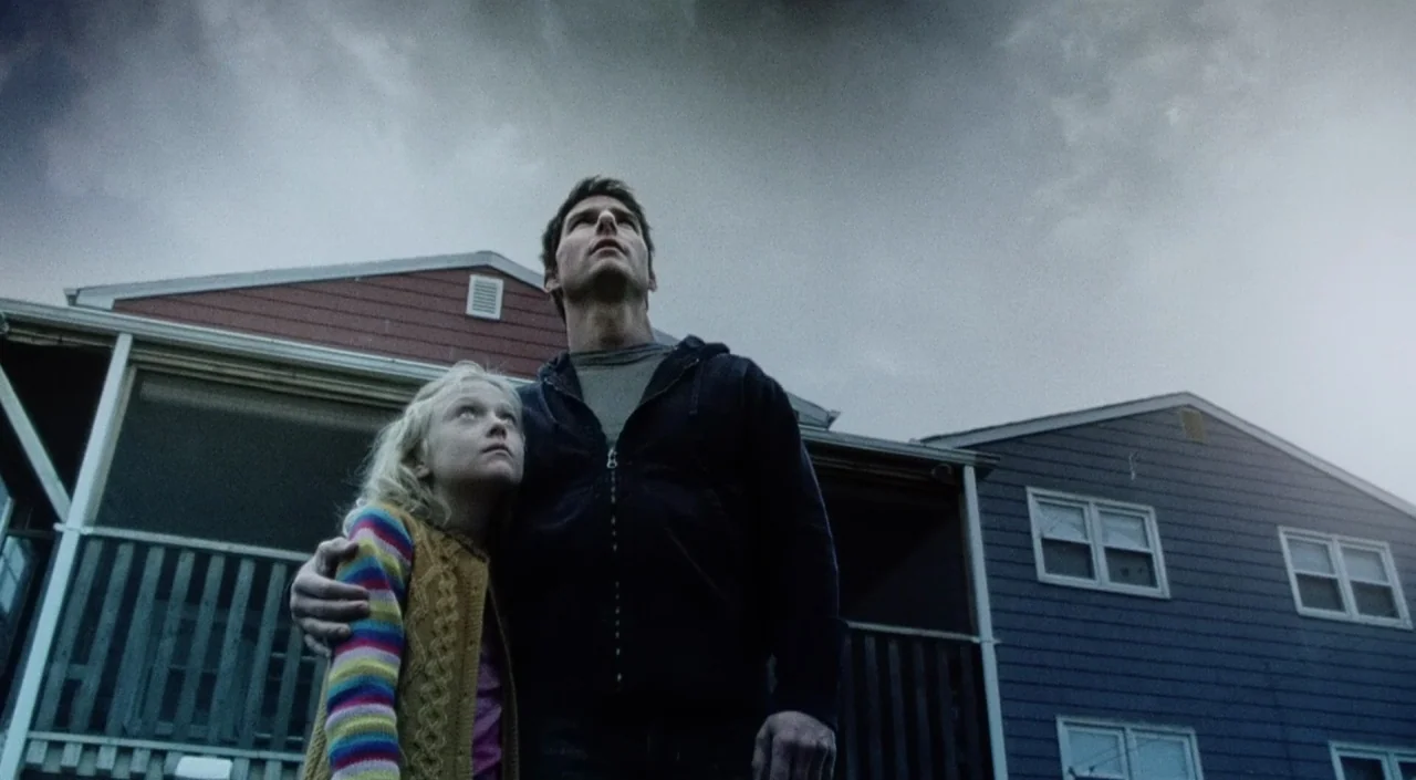 War of the Worlds (2005) movie still: medium — A man and child stand before a suburban house under a dark, overcast sky. They look upward at the sky…