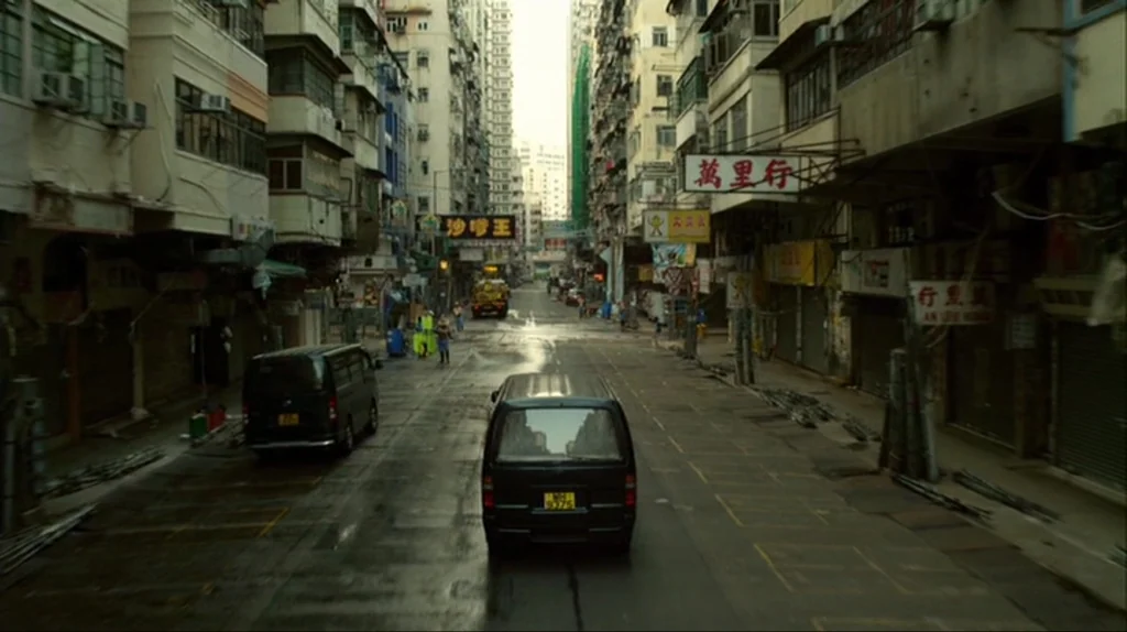 Contagion (2011) movie still: establishing — A dense Hong Kong street lined with towering residential buildings features numerous hanging commercial…