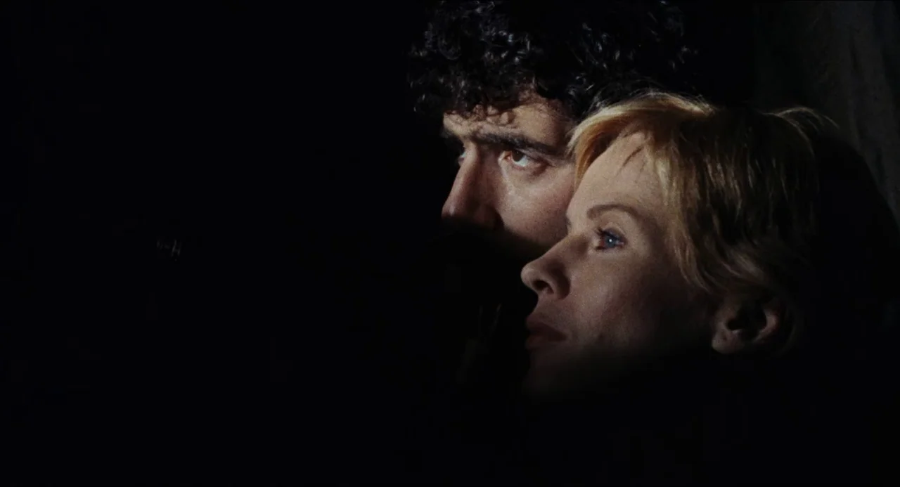 The Touch (1971) movie still: closeup — A man and a woman are positioned in a dark environment with no visible surroundings. They sit together with…