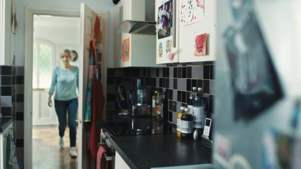 You Might Get Lost (2021) movie still: medium — A residential interior features black tiled counters and cabinets covered in children's drawings. A…