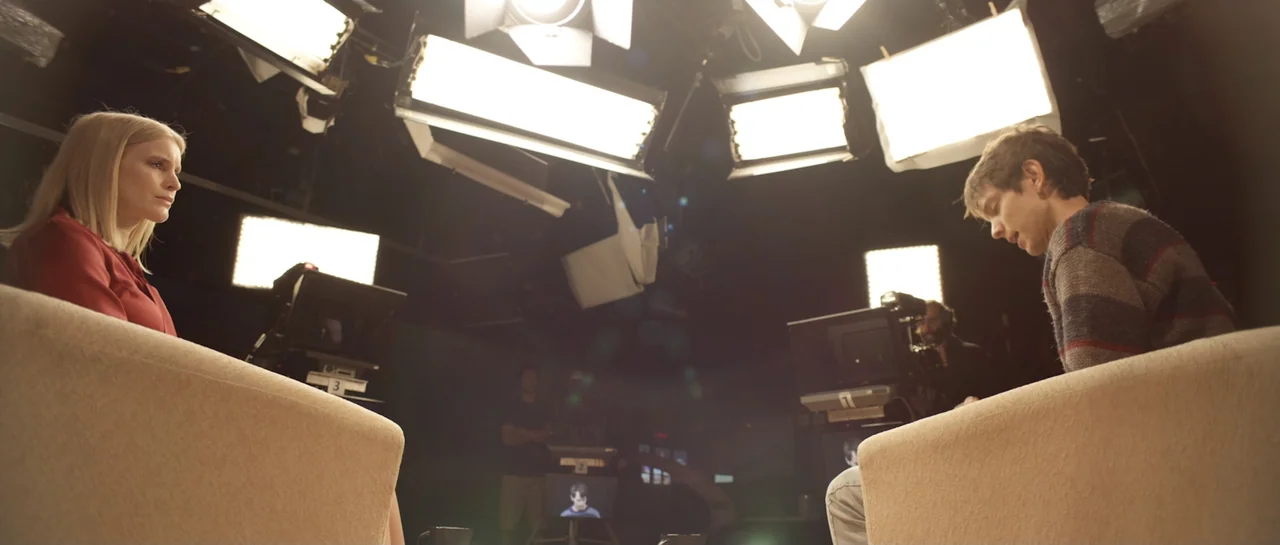 La presencia (2012) movie still: wide — A television studio set contains two beige armchairs facing each other under bright lights. A blonde woman…