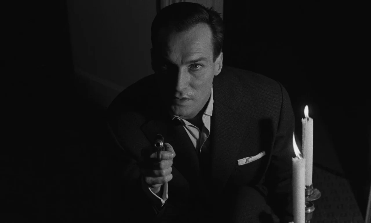 Witness In The City (1959) movie still: medium — A dimly lit interior space is illuminated primarily by two tall burning candles. A man in a suit…