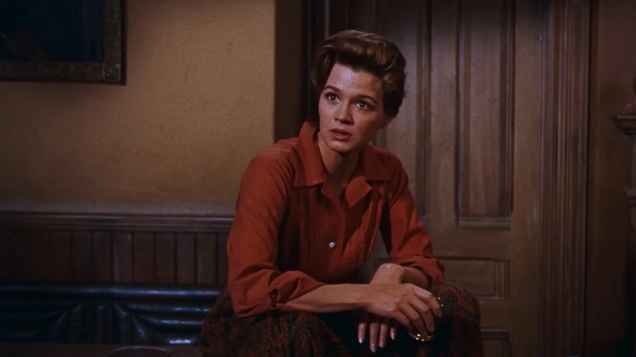 Rio Bravo (1959) movie still: medium — A dimly lit room features wood-paneled walls and a matching door in the background. A woman sits in the…