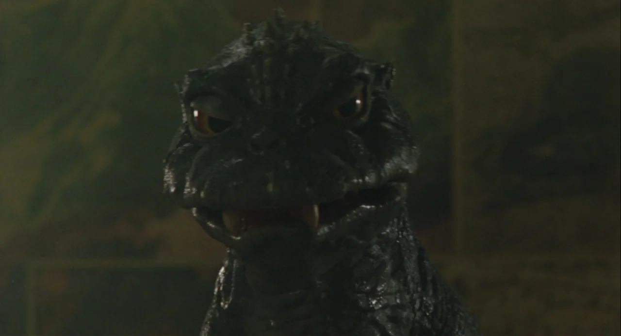 Godzilla vs. Mechagodzilla II (1993) movie still: closeup — A dark, indistinct environment frames the head and shoulders of a reptilian monster. The…
