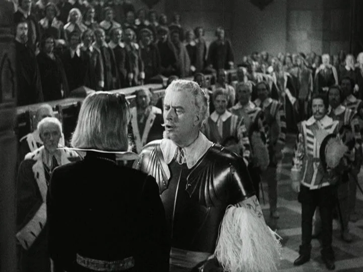 Queen Christina (1933) movie still: medium — A crowded stone room filled with onlookers dressed in 16th-century style garments. An older man in…