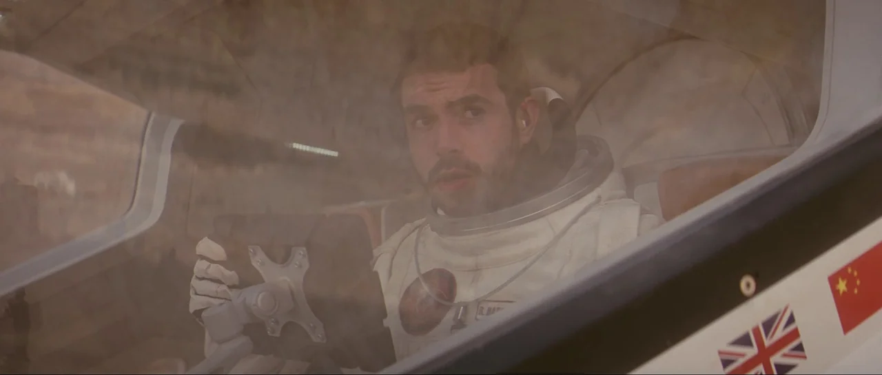 The Last Days On Mars (2013) movie still: closeup — A man sits inside a spacecraft cockpit viewing a desert landscape through the window. The pilot…