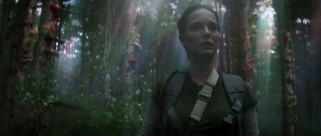 Annihilation (2018) movie still: medium — A dense woodland environment with tall trees covered in strange colorful fungal growths. A woman wearing a…