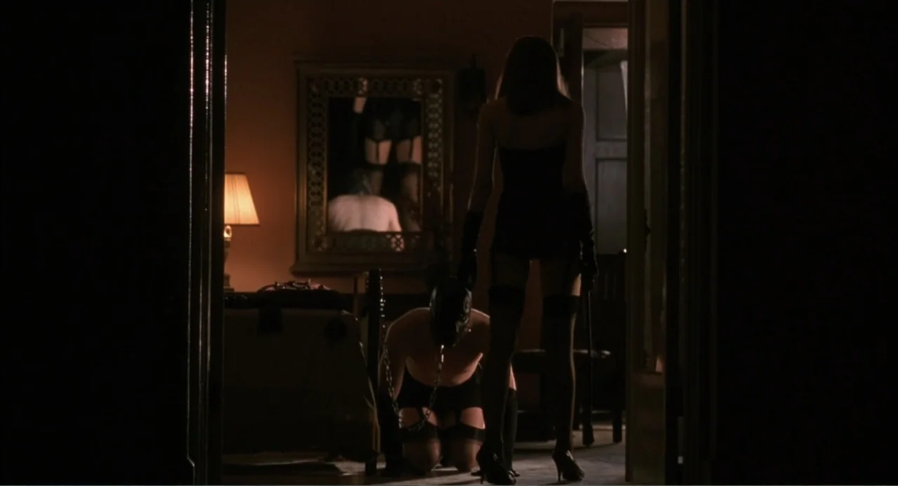 Wild Orchid II: Two Shades of Blue (1991) movie still: fullbody — A dimly lit room contains a person in a mask kneeling on the floor. A woman in a…