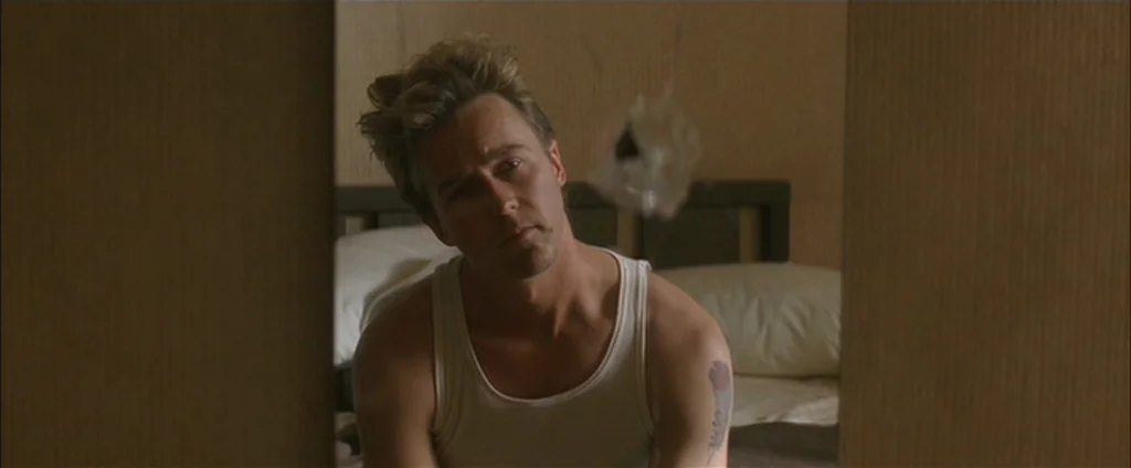 Down In The Valley (2005) movie still: medium — A man sits in a sparse, beige-walled space in front of a simple frame. He stares straight forward…