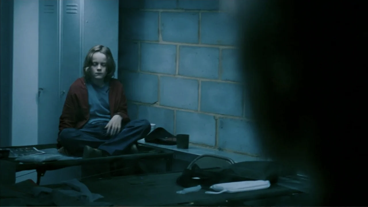28 Weeks Later (2007) movie still: medium — A dimly lit room with cinder block walls and metal locker units against one side. A young girl sits…