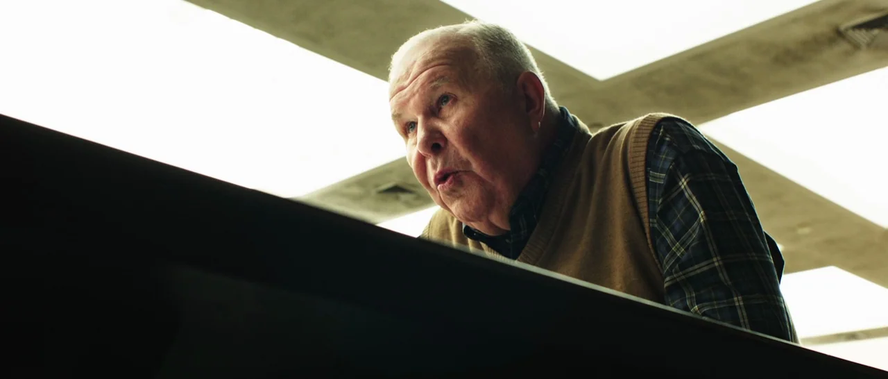 Rampart (2011) movie still: medium — An office interior features a drop ceiling with recessed, glowing square fluorescent light panels. An elderly…
