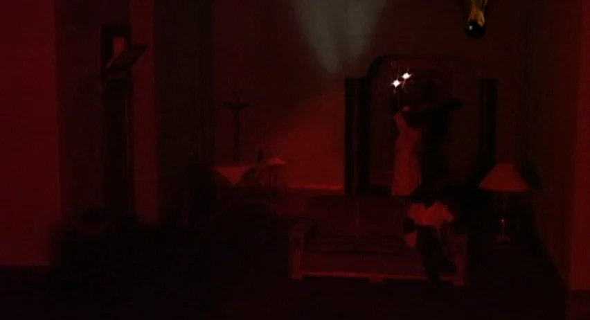 Inland Empire (2006) movie still: wide — A sparsely furnished room is shrouded in darkness and a heavy red light. A lone sofa sits center frame…
