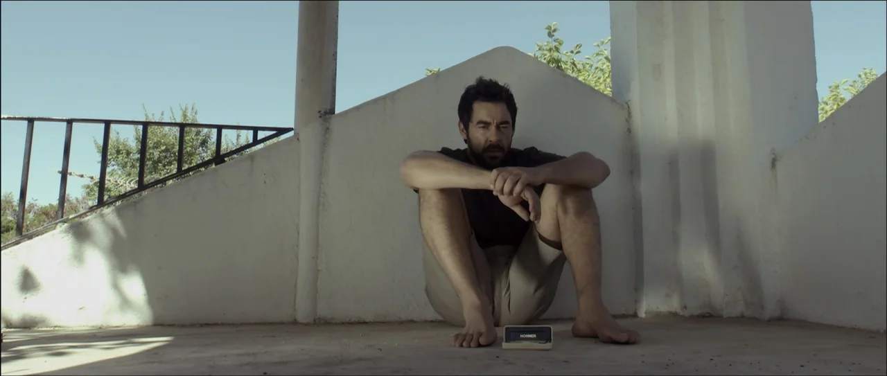 Otro verano (2013) movie still: medium — A man sits on a concrete floor in a white concrete structure. The man sits cross-legged while facing a…