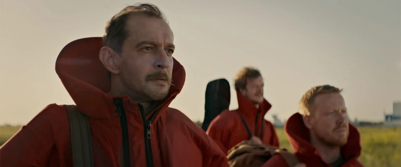 In the Line of Duty: Smoke Jumpers (1996) movie still: medium — An open grassy area provides the background for three men standing in a row. They…