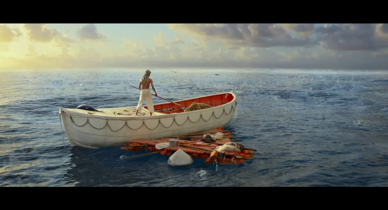 Life of Pi (2012) movie still: wide — A white wooden lifeboat tethered to a small wooden raft floats on calm water. A young man stands in the…