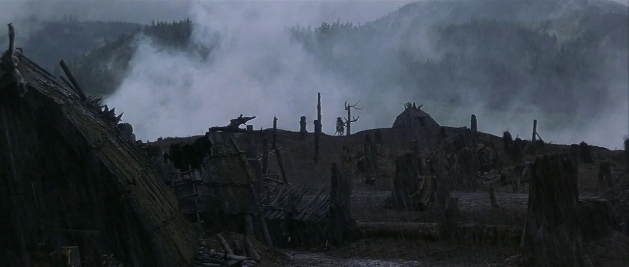 The 13th Warrior (1999) movie still: establishing — A rain-swept landscape features several primitive wooden structures and jagged tree stumps under…