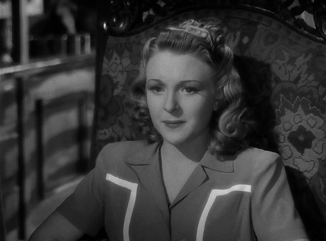 The Wolf Man (1941) movie still: medium — An interior space features an ornate patterned fabric chair with wood trim. A woman sits in the chair…