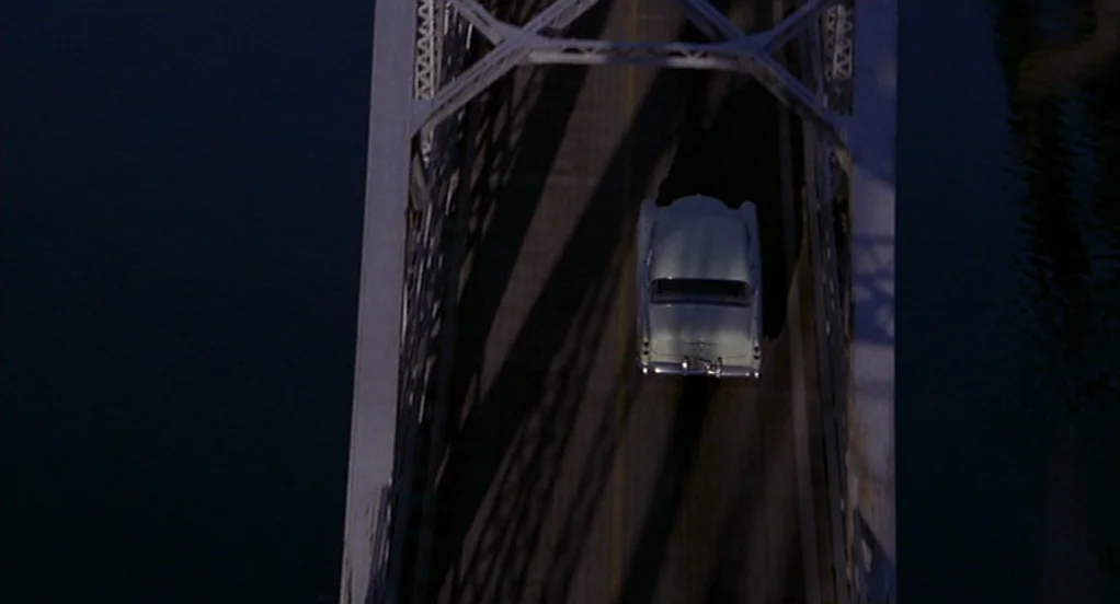 The Indian Runner (1991) movie still: wide — A dark metal truss bridge crosses a expanse of deep, shadowed water at night. A light-colored vintage…