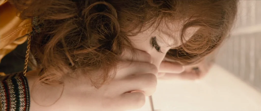 The Look of Love (2013) movie still: closeup — A woman leans over a light-colored surface with auburn hair obscuring part of her face. She holds a…